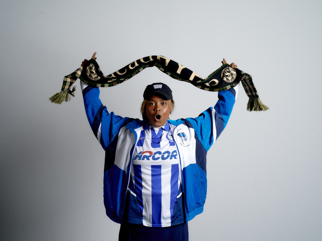 Person wearing a sports jersey and holding a deadHYPE Tartan Scarf (Camo) against a gray background