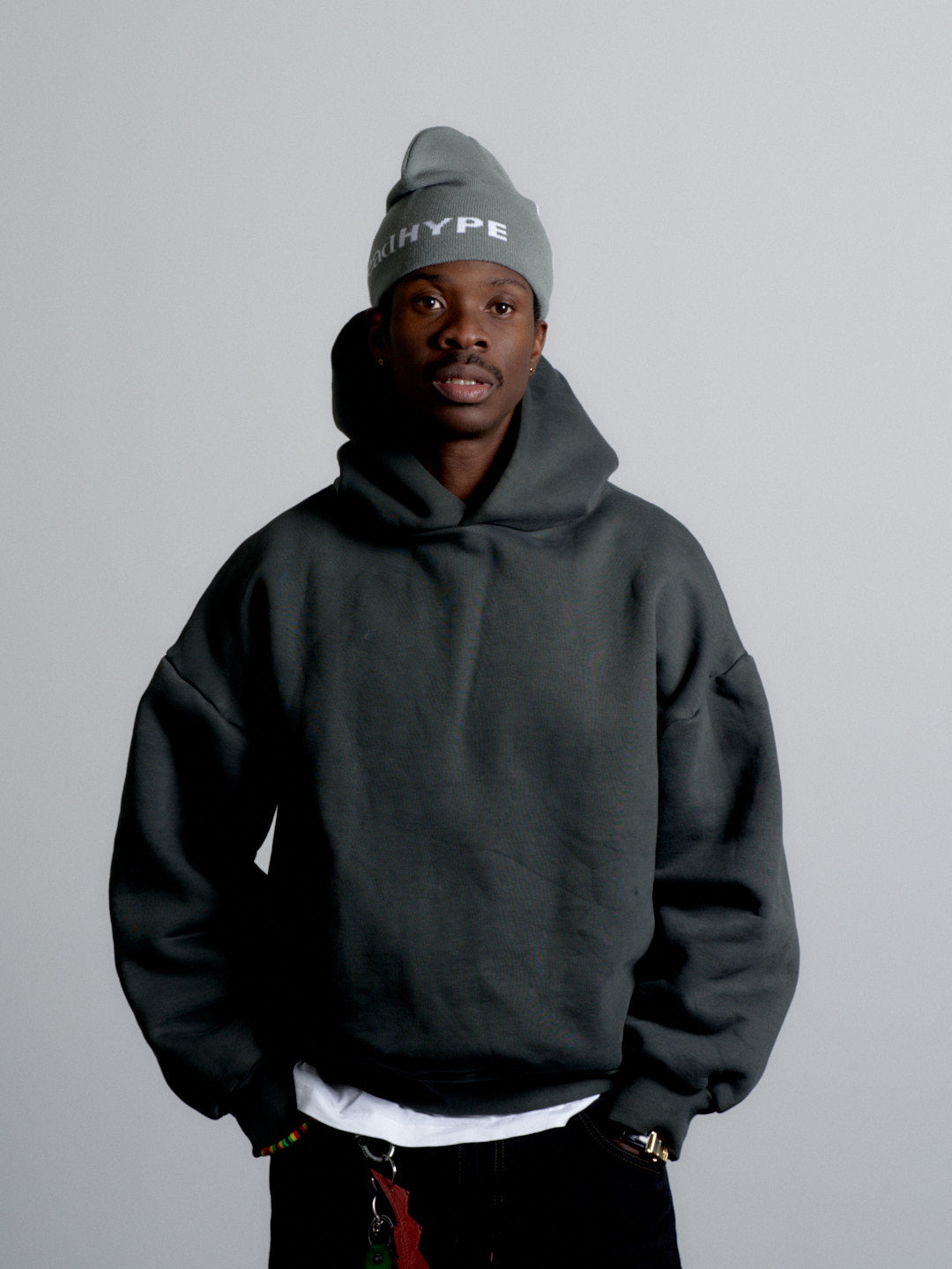 Man wearing a black hoodie and gray beanie with 'HYPE' text on a plain background